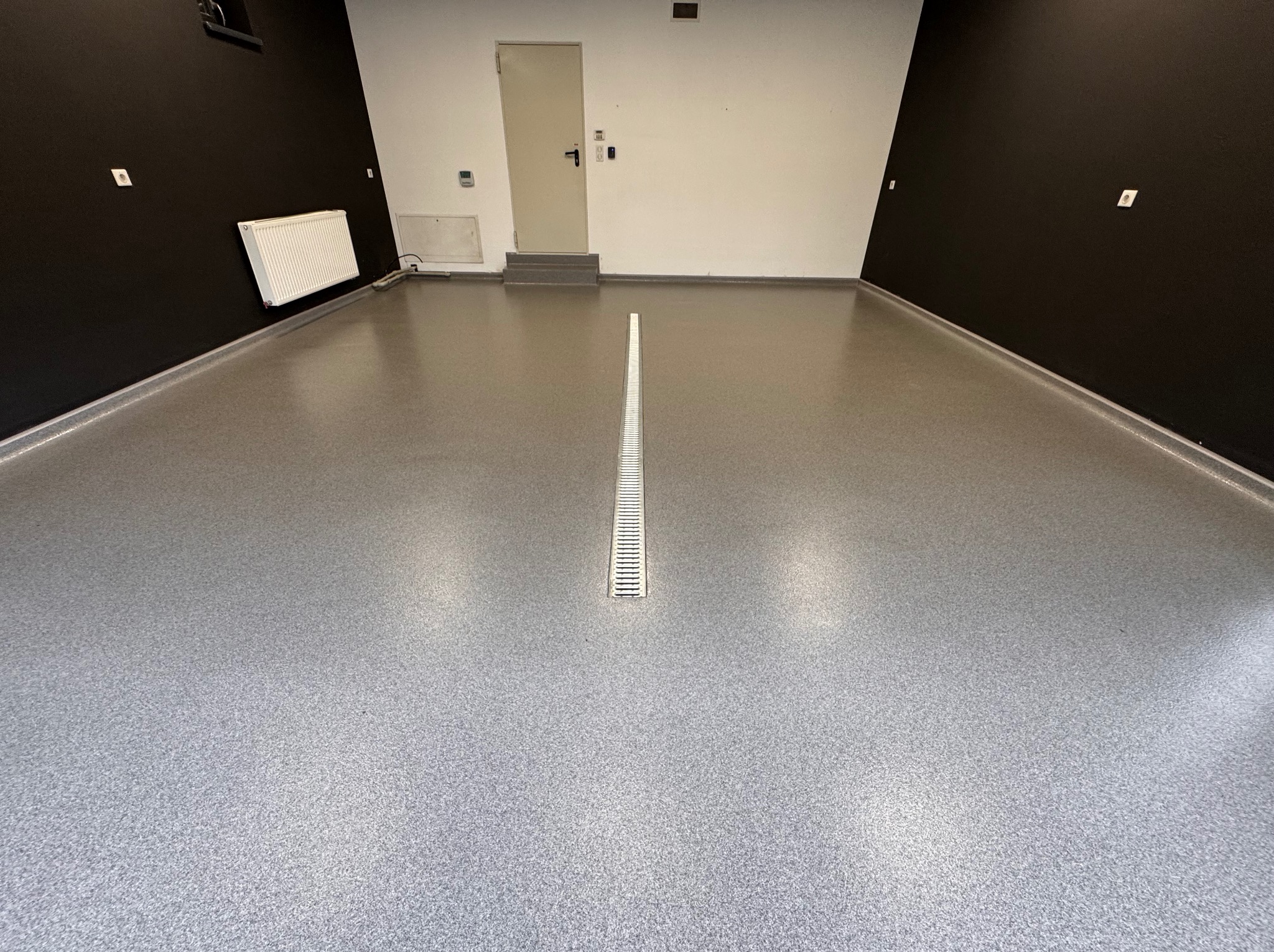 Szara posadzka z odpływem liniowym w pomieszczeniu z czarnymi i białymi ścianami.