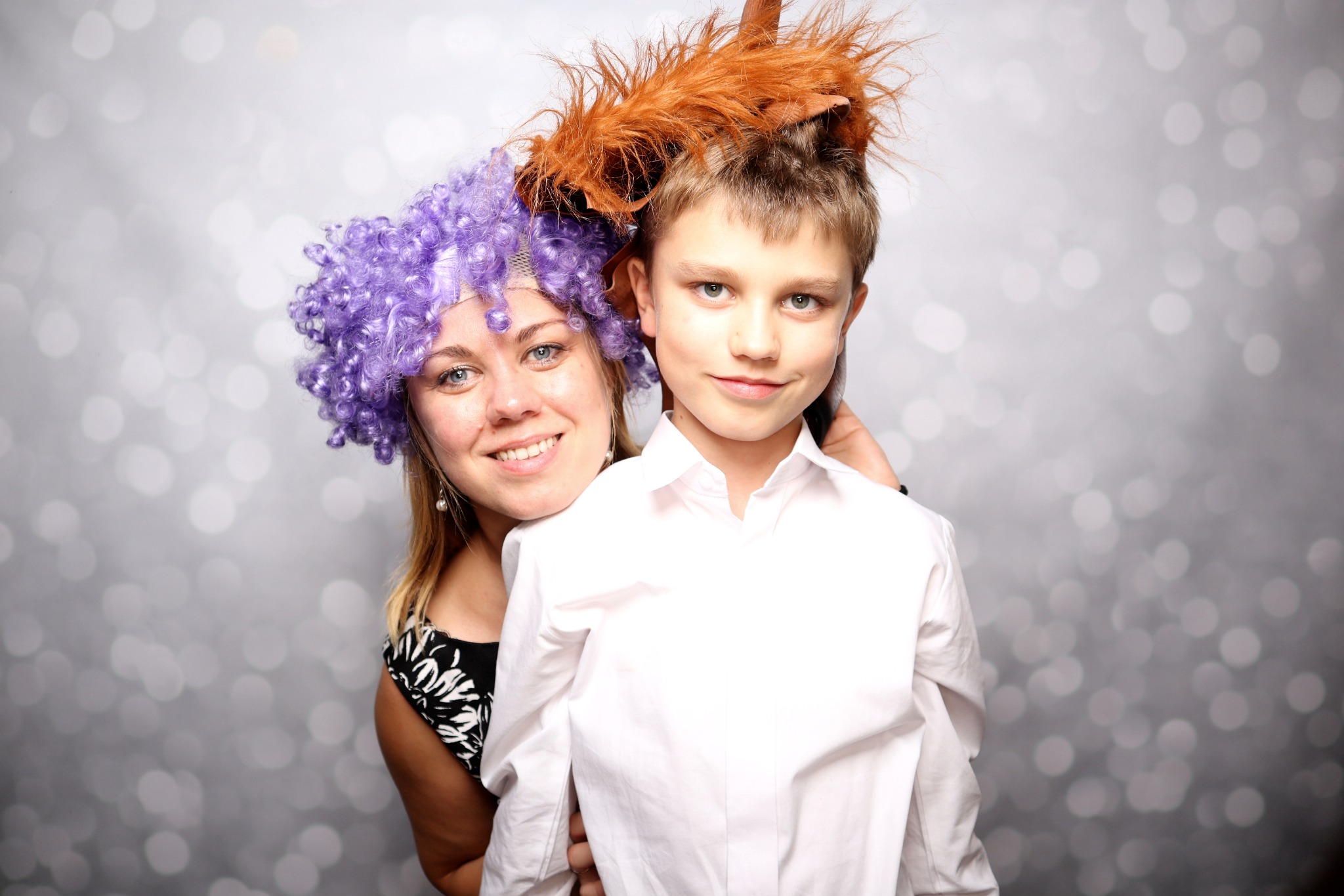 Kobieta w fioletowej peruce i chłopiec w kostiumie konia pozują na tle srebrnego, błyszczącego tła.