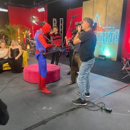 Twój Dj Maciej DJ SPIDER - Scena z muzykiem w kostiumie Spider-Mana grającym na keytarze podczas nagrania telewizyjnego. W tle zespół, publiczność i ekipa filmowa.