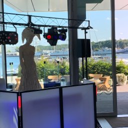 Twój Dj Maciej DJ SPIDER - Dekoracja rzeźbiarska pod oświetleniem eventowym, widok na port i morze przez przeszkloną ścianę. Scena z konsoletą DJ-ską w klubie.