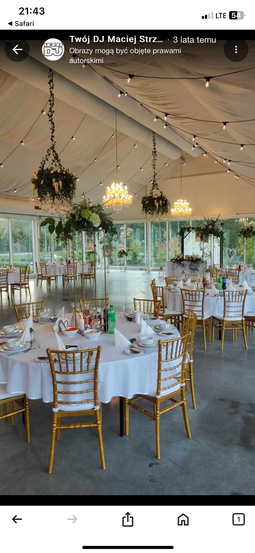 Elegancka sala bankietowa z okrągłymi stołami, złotymi krzesłami, kwiatowymi dekoracjami pod sufitem i oświetleniem girlandami. Widok na zewnątrz przez szklane ściany.