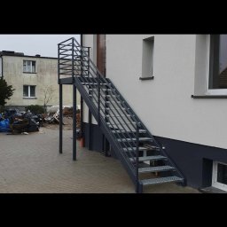 GoHouse Usługi spawalniczo ślusarskie - Zewnętrzne schody metalowe z ażurową balustradą prowadzące do drzwi na piętrze budynku, widoczne metalowe stopnie z kratki.