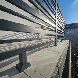 GoHouse Usługi spawalniczo ślusarskie - Nowoczesna balustrada balkonowa z poziomych, metalowych profili w kolorze grafitowym, zamontowana na płytkach tarasowych w słoneczny dzień.