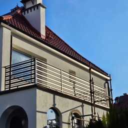 GoHouse Usługi spawalniczo ślusarskie - Nowoczesna balustrada balkonowa z poziomych profili zamontowana w budynku z czerwoną dachówką, widoczne rusztowania.