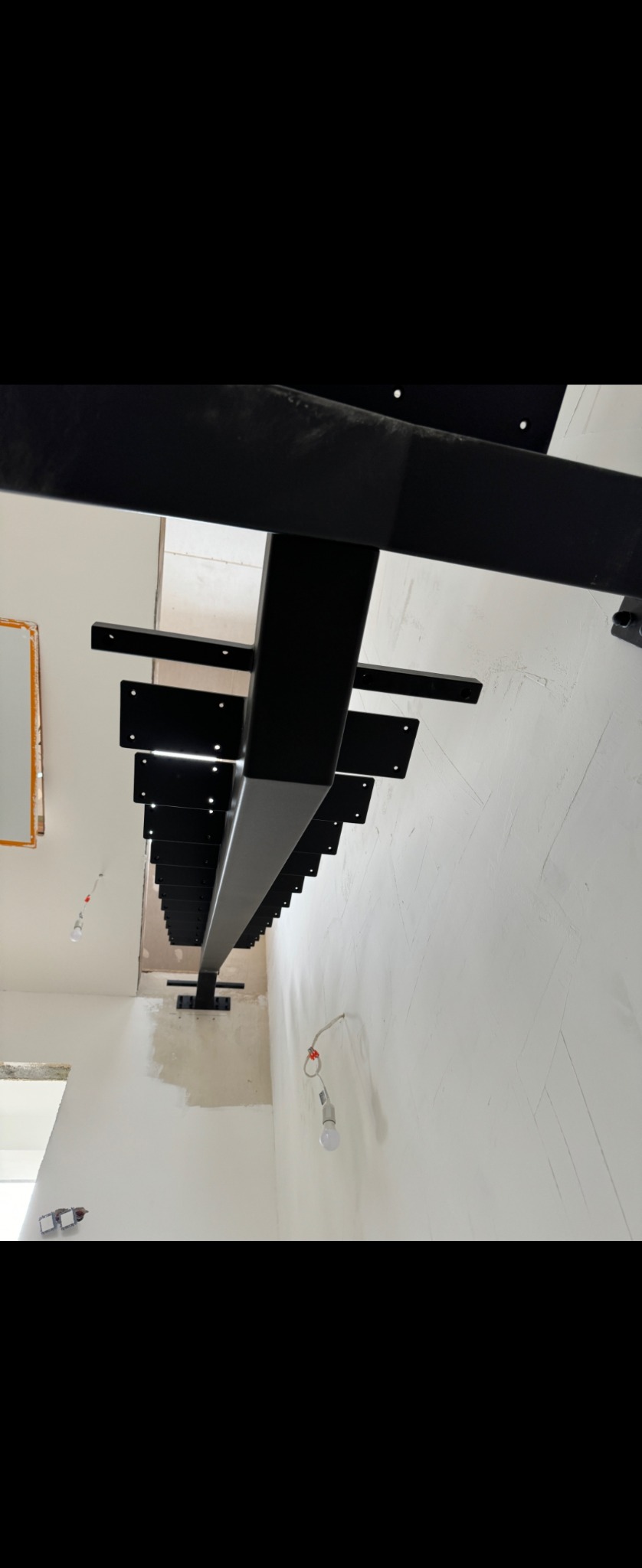 Metalowa konstrukcja schodów w trakcie montażu, widoczne elementy mocujące do ściany, surowy stan wykończenia wnętrza.