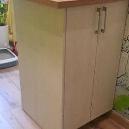 Wykończona szafka kuchenna z blatem z drewna, jasne fronty szafek z podłużnymi uchwytami, na blacie szklana płyta, w tle wzorzysta tapeta z motywem owoców i wody.