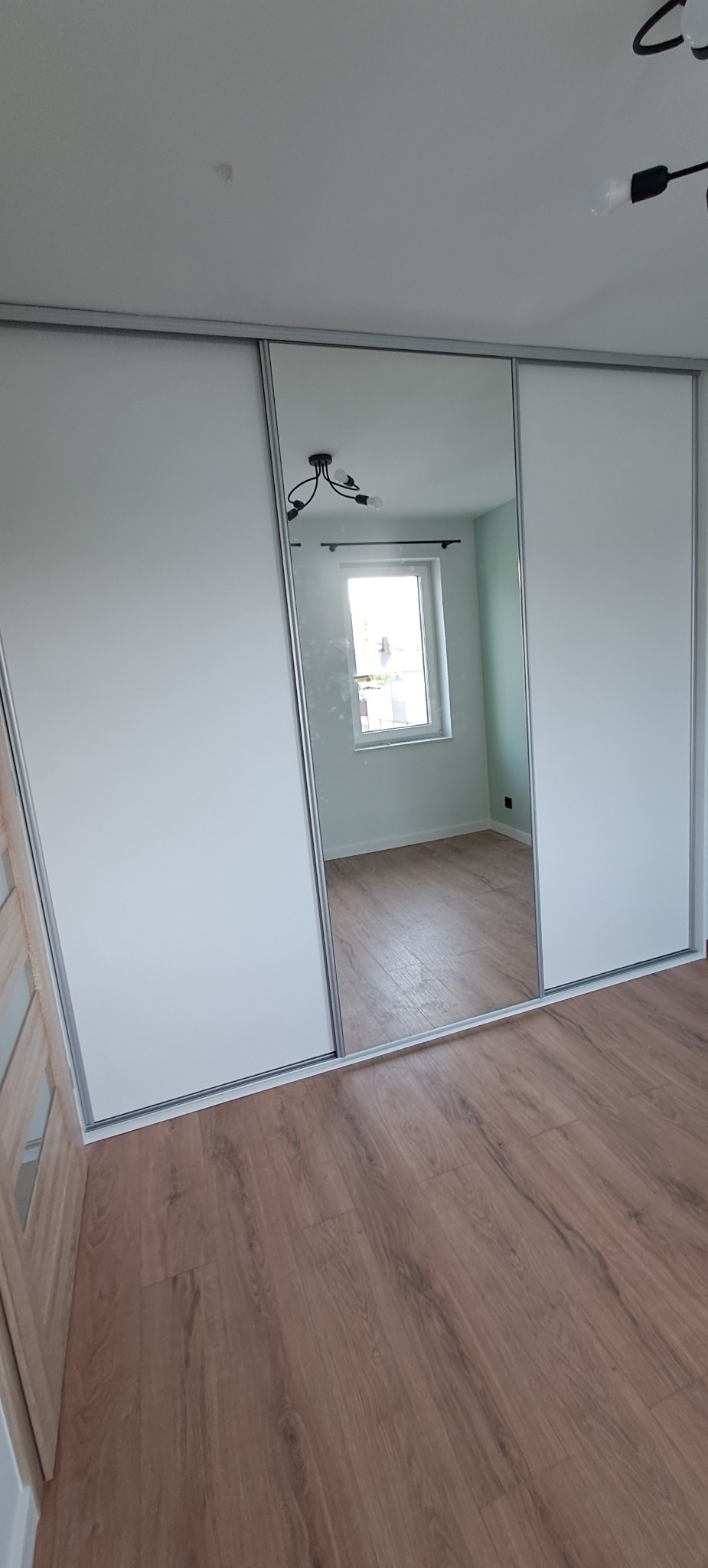 Szafa wnękowa z przesuwnymi drzwiami z lustrem w mieszkaniu w Zielonej Górze, odbicie okna i lampy w lustrze.