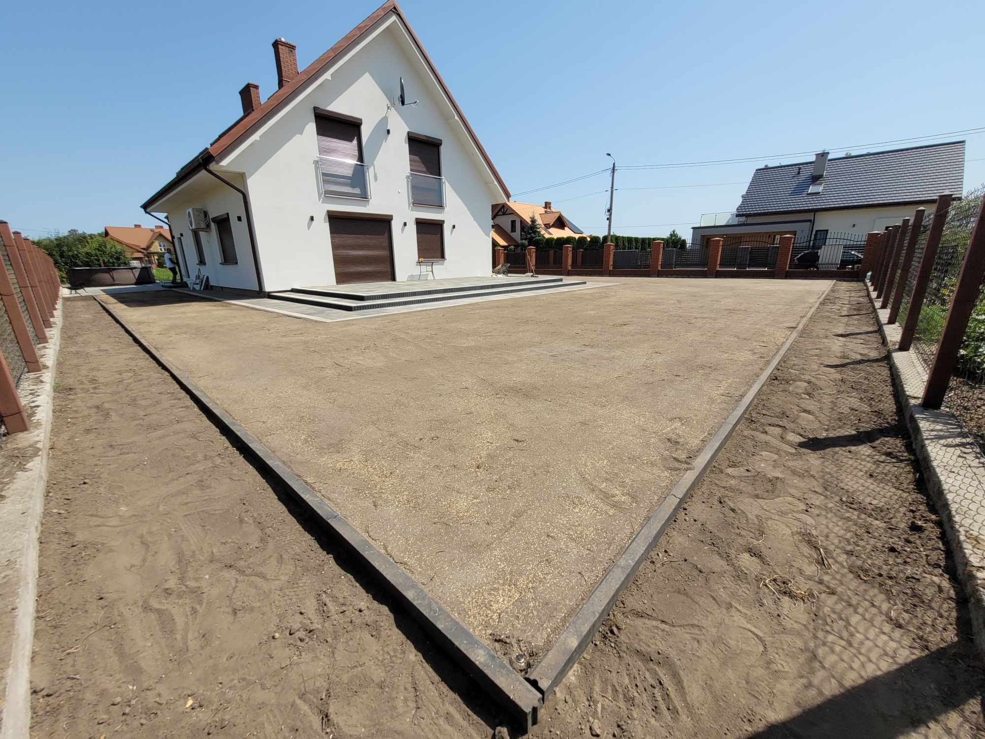 Przygotowany teren pod trawnik przed nowoczesnym domem jednorodzinnym, widoczne obrzeża i wyrównana powierzchnia z posianą trawą, ogrodzenie w tle.