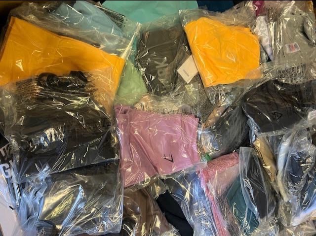 Paczka odzieży markowej w folii, widoczne różne kolory i fasony, gotowe do wysyłki.