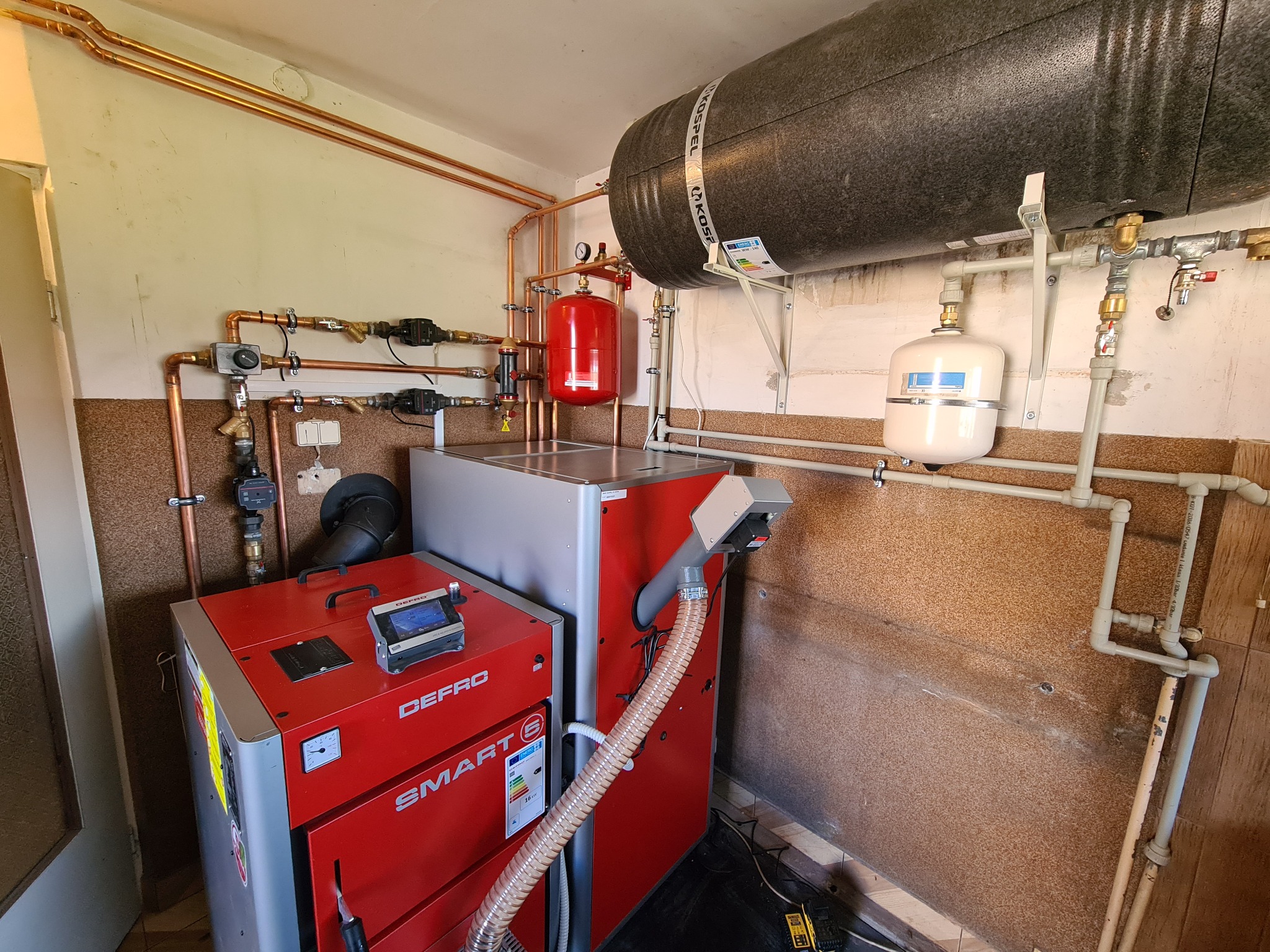 Kotłownia z dwoma kotłami Defro Smart G, zbiornikiem akumulacyjnym Kospel i kompletną instalacją z miedzianych rur, zaworów i elementów pomiarowych.