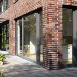 Szklane drzwi przesuwne w Kujakowicach Górnych z ciemną ramą, wbudowane w ścianę z czerwonej cegły, widoczne z zewnątrz na drewnianym tarasie.
