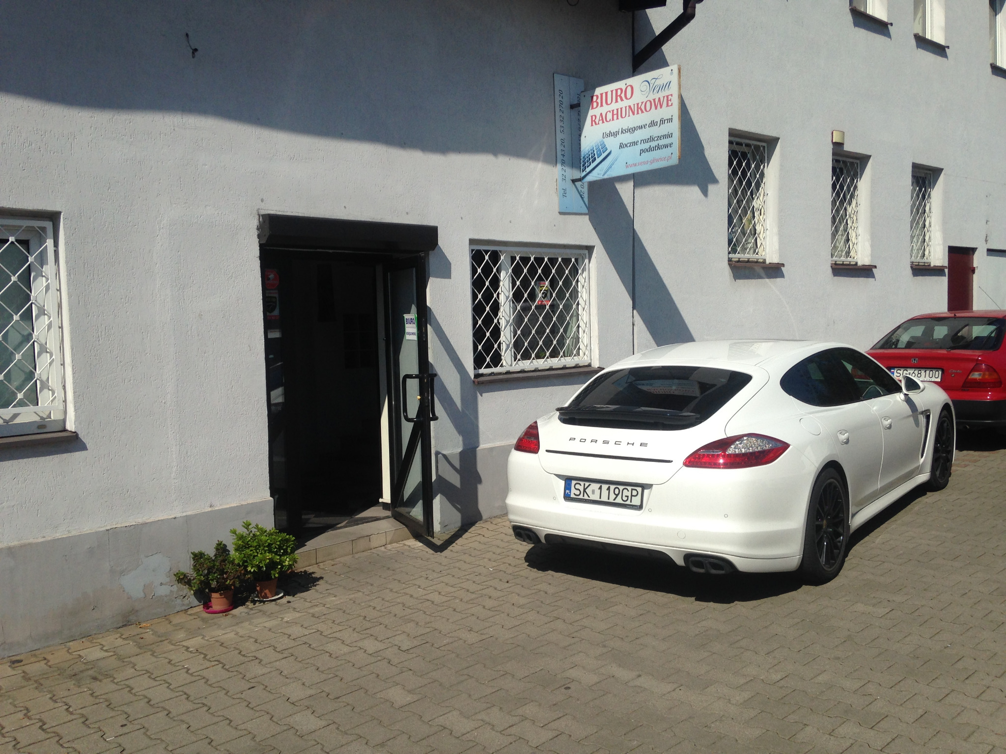 Białe Porsche zaparkowane przed wejściem do Biura Rachunkowego Vena w Gliwicach, z widoczną tablicą informacyjną o usługach księgowych i rocznych rozliczeniach podatkowych.