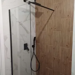 Nowoczesna kabina prysznicowa z czarnymi elementami armatury na tle płytek imitujących marmur i drewno.