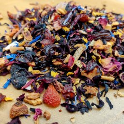 Herbaty i Kawy Świata - Mieszanka suszonych owoców i kwiatów do zaparzania herbaty, widoczne fragmenty hibiskusa, skórki pomarańczy i płatki bławatka na jasnym tle.