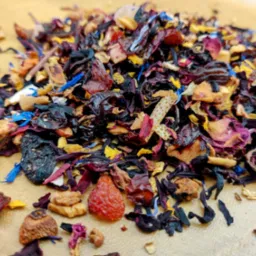 Mieszanka suszonych owoców i kwiatów do zaparzania herbaty, widoczne fragmenty hibiskusa, skórki pomarańczy i płatki bławatka na jasnym tle.