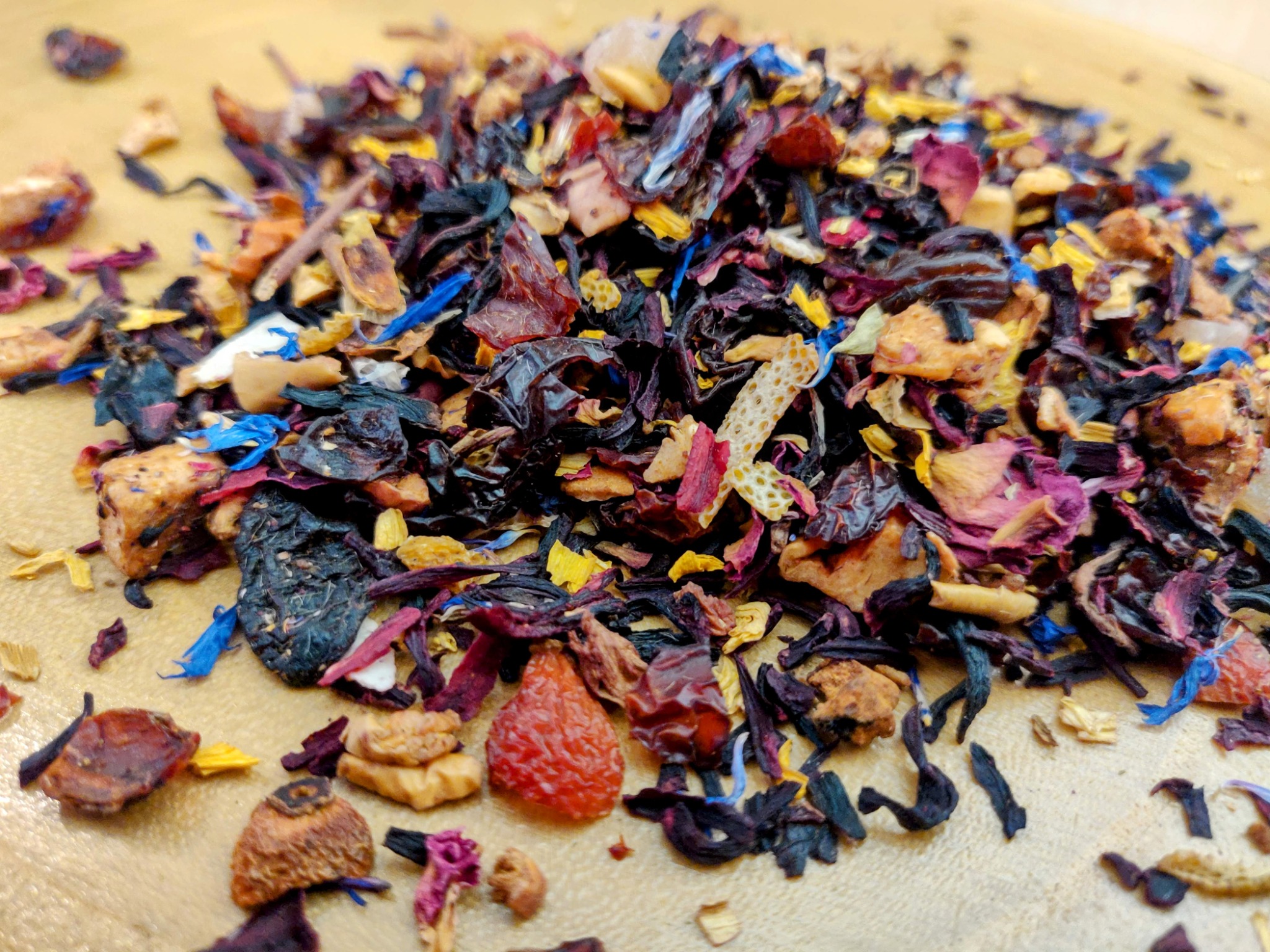 Mieszanka suszonych owoców i kwiatów do zaparzania herbaty, widoczne fragmenty hibiskusa, skórki pomarańczy i płatki bławatka na jasnym tle.