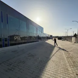 Mycie przeszklonej fasady budynku komercyjnego z użyciem lancy teleskopowej. Osoba w trakcie pracy, widoczne refleksy słońca na szklanych powierzchniach.