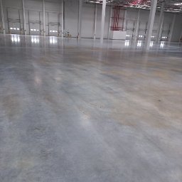 Paweł Przybyszewski-specjalistyczne doczyszczanie - Polerowana, betonowa posadzka przemysłowa w hali magazynowej z widocznymi bramami segmentowymi i instalacjami pod sufitem.