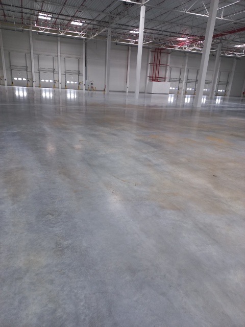 Polerowana, betonowa posadzka przemysłowa w hali magazynowej z widocznymi bramami segmentowymi i instalacjami pod sufitem.