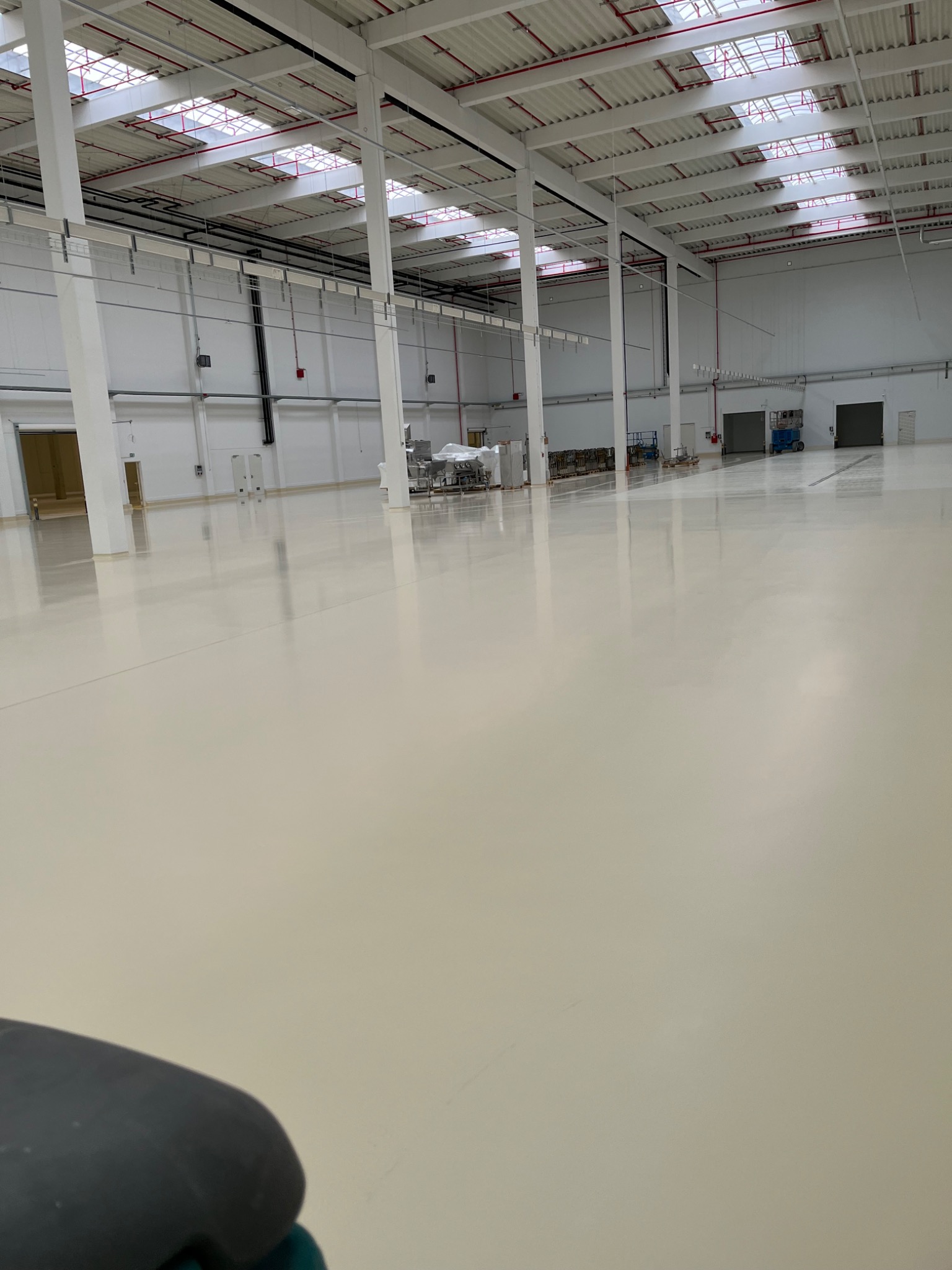 Błyszcząca, jasna posadzka w hali przemysłowej w Świebodzinie po niedawnym czyszczeniu, widoczne odblaski światła od okien dachowych i elementów konstrukcyjnych sufitu.