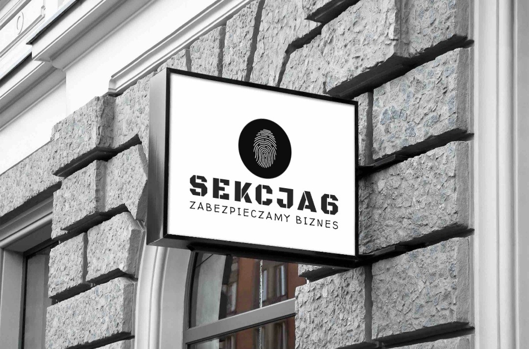 Szyld firmy ochroniarskiej 'SEKCJA6' z odciskiem palca na szarym, kamiennym murze budynku.