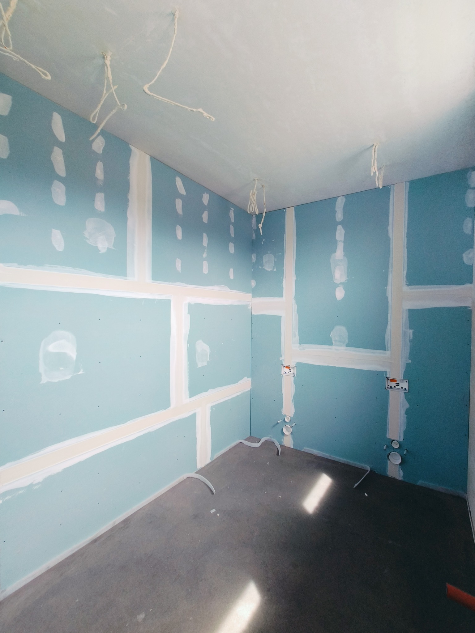 Wnętrze w trakcie wykańczania: ściany z płyt karton-gips, widoczne łączenia szpachlowane, wystające kable, przygotowane podłoże.