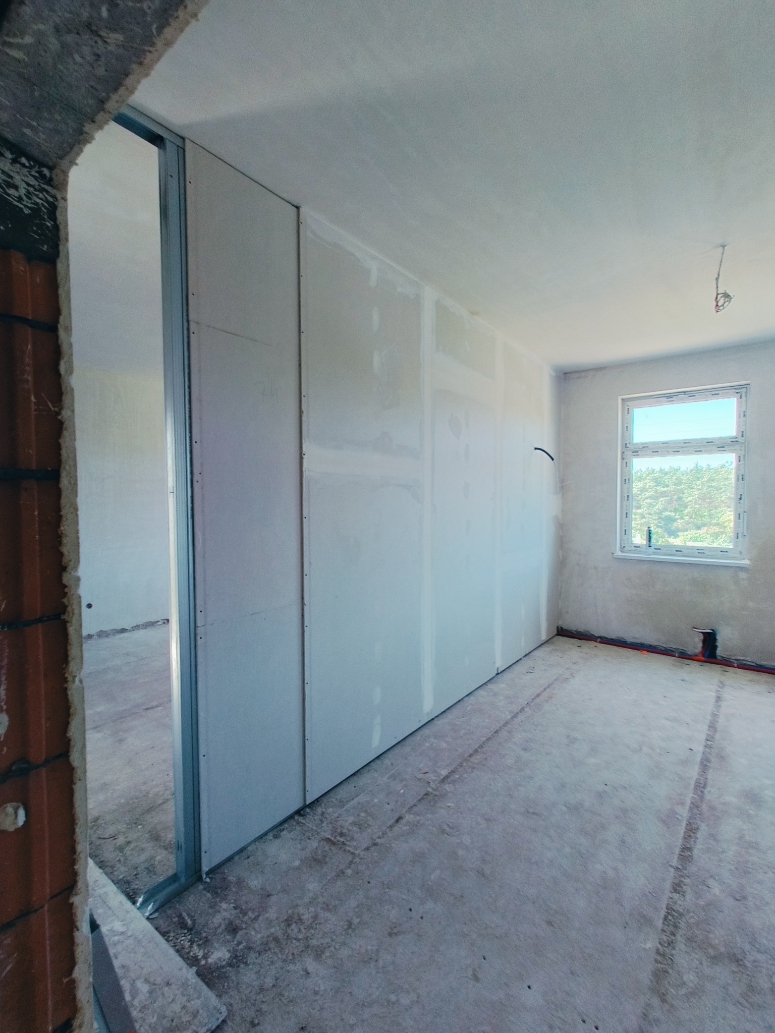 Wnętrze w trakcie montażu ścian działowych z płyt gipsowo-kartonowych na metalowym stelażu, widoczne okno i surowy beton na podłodze.