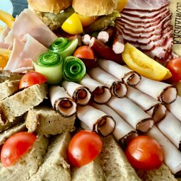 Karczma Słowiańska - Bogato zaaranżowana deska przekąsek: mini burgery, wędliny w rolkach, plastry szynki, pomidorki koktajlowe, ogórki w rozetki i pieczywo. Idealna propozycja na catering.