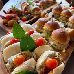 Karczma Słowiańska - Drewniana deska z mini burgerami, kanapeczkami i przekąskami, udekorowana listkami i pomidorkami koktajlowymi. Elegancki catering na imprezę firmową.