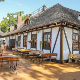 Zewnętrzny widok restauracji w stylu rustykalnym z drewnianymi stołami i ławkami na tarasie, dekoracje świąteczne na oknach, parasole w tle.