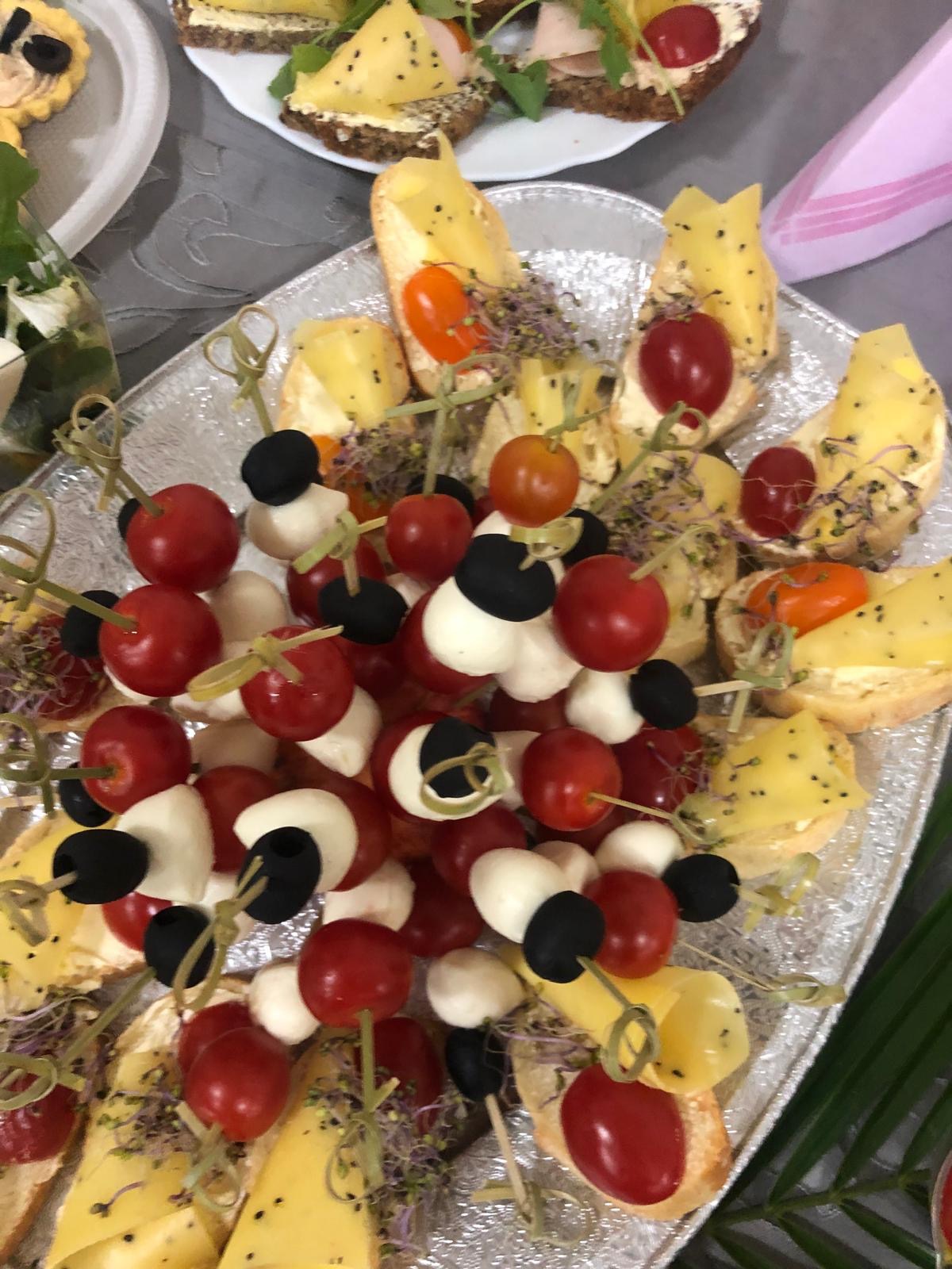 Elegancka srebrna patera z apetycznymi przekąskami: koreczki z pomidorkami, oliwkami i mini-mozzarellą oraz kanapki z serem i kiełkami. Idealne na przyjęcie.