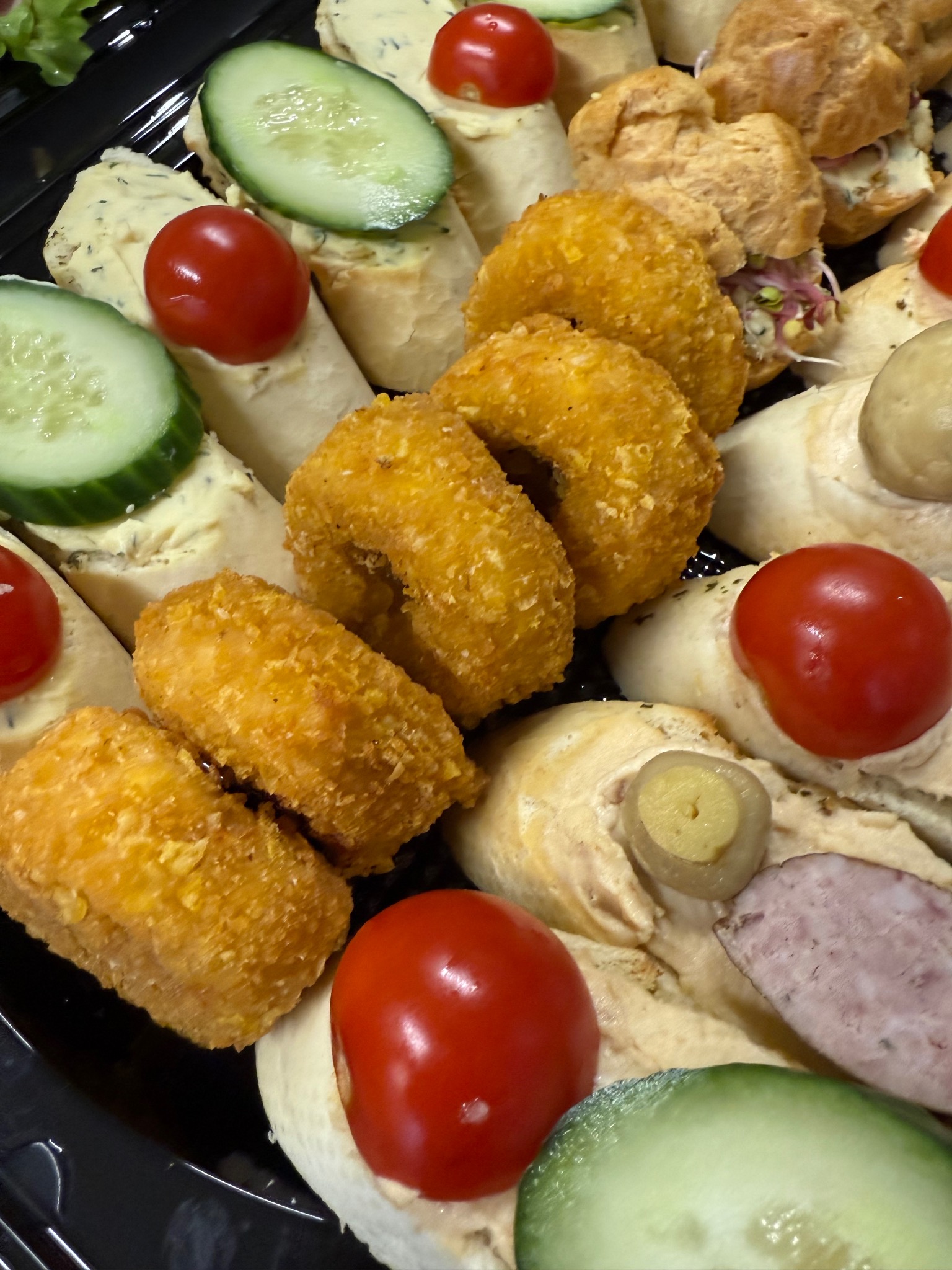 Elegancki catering: kanapeczki z pomidorkami, ogórkiem, pastą, krokiety i mini-ptysie na czarnym talerzu. Idealne na firmowe przyjęcie.