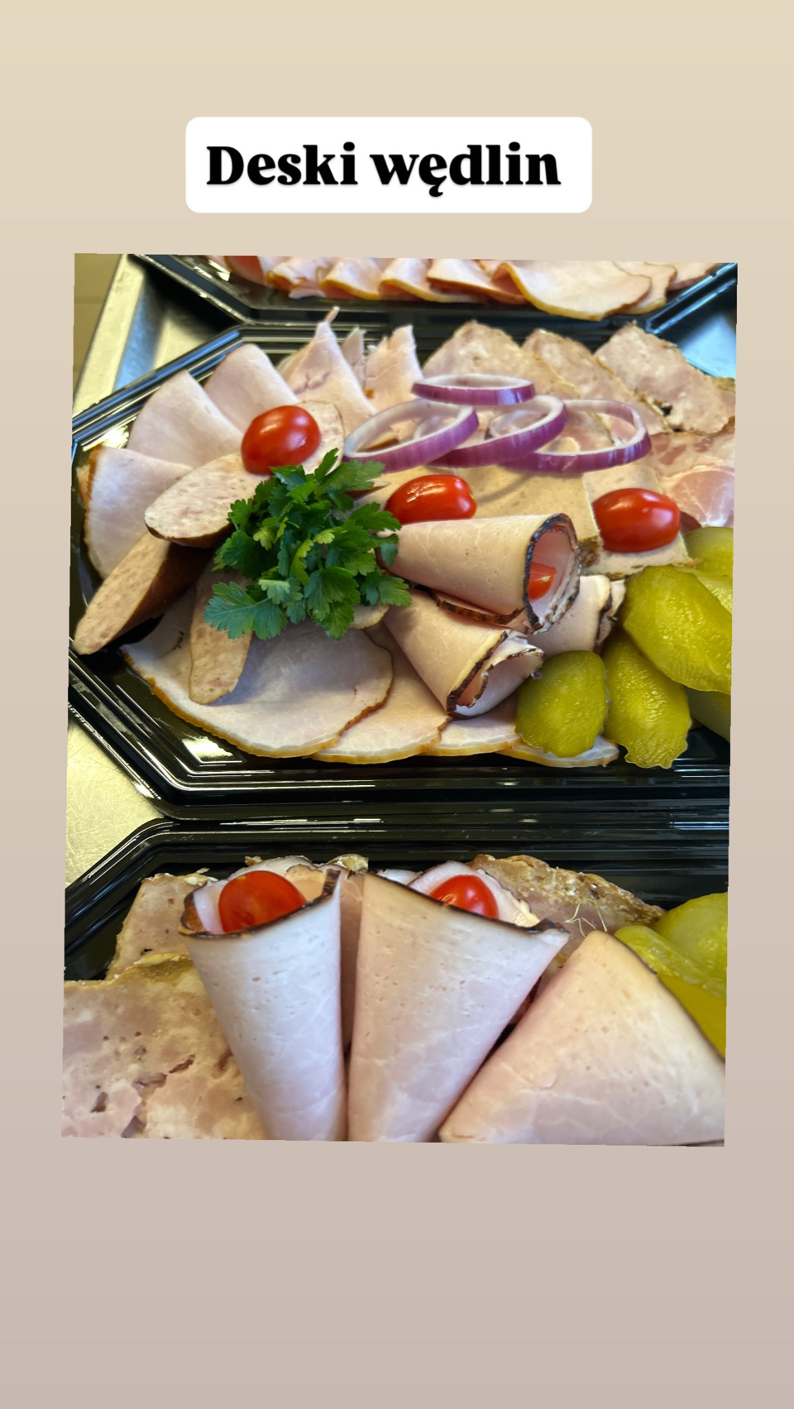 Dwie deski wędlin na czarnych tacach, z roladkami szynki z pomidorkiem, ogórkami konserwowymi, plastrami cebuli i natką pietruszki.