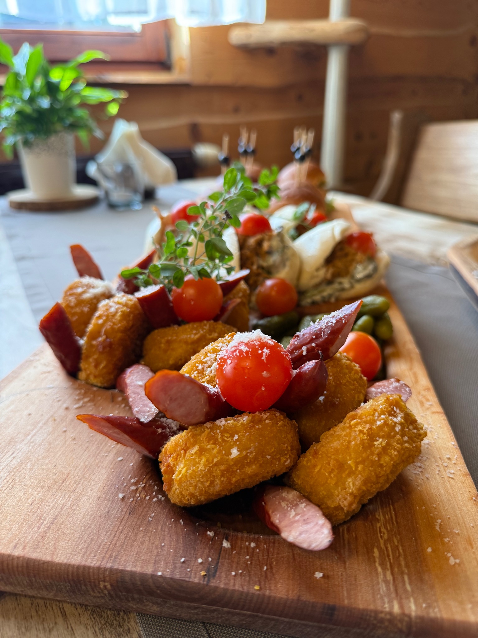 Drewniana deska z przekąskami: krokiety, kiełbasa, pomidorki koktajlowe, ogórki konserwowe i mini-burgery. Dekoracja z ziół. Idealne na catering.