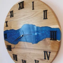 Okrągły zegar ścienny z jasnego drewna z czarnymi cyframi rzymskimi i wstawką z niebieskiej żywicy imitującą rzekę, wskazówki ustawione na godzinę 2:58.
