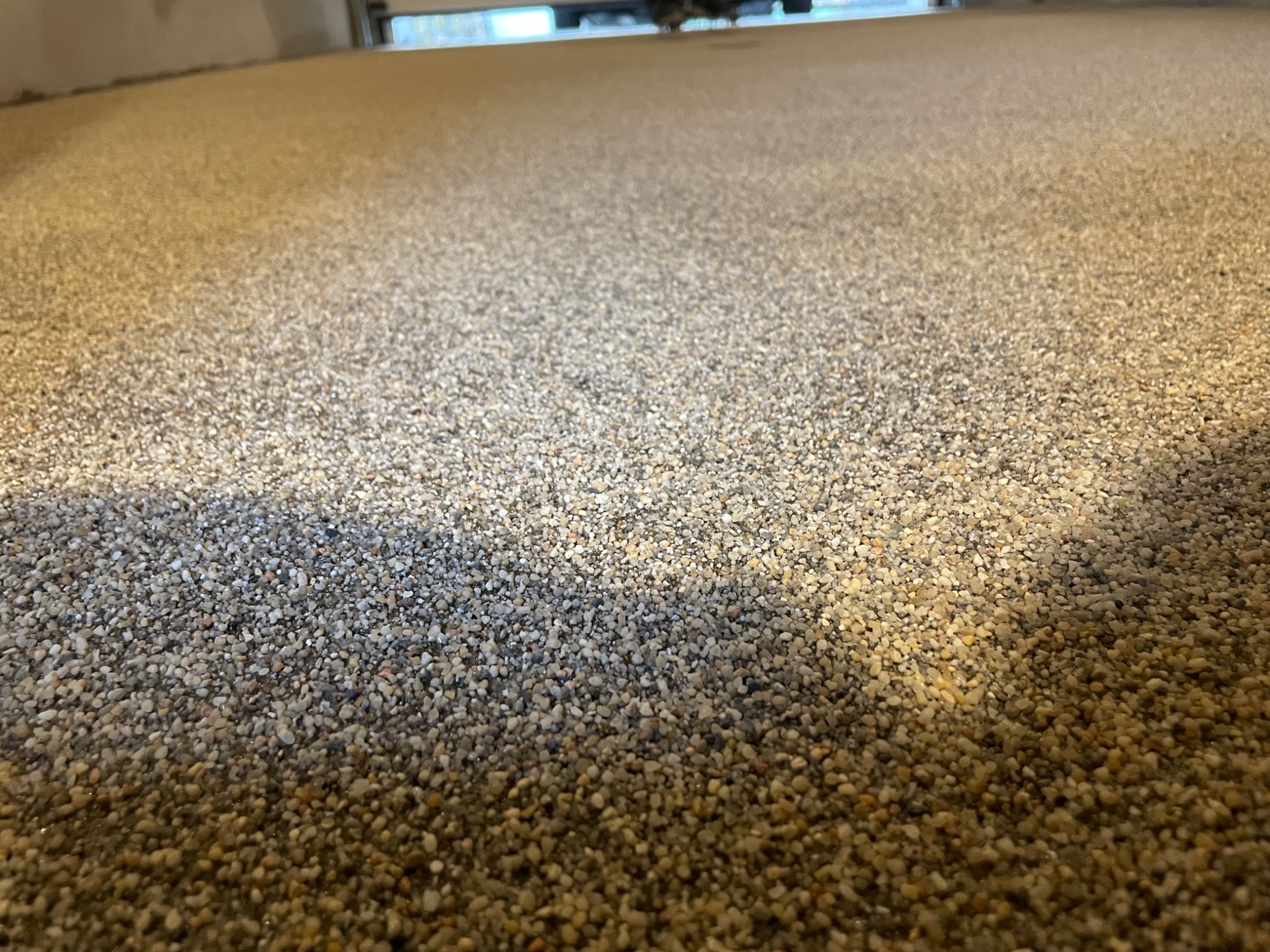 Posadzka żywiczna z drobnym kruszywem kwarcowym w ciepłych odcieniach beżu i szarości, widoczna z niskiej perspektywy, z delikatnym cieniem padającym na powierzchnię i rozmytym tłem.