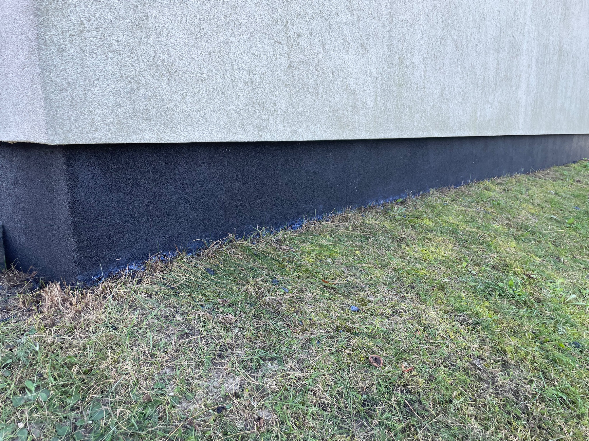 Ocieplenie fundamentu budynku z widoczną warstwą izolacyjną w kolorze grafitowym, stykającą się z trawnikiem.