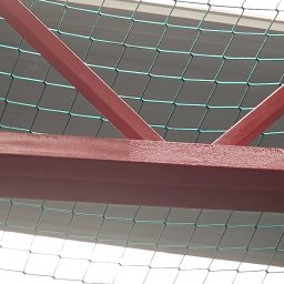 DECOLUX - Metalowa konstrukcja pomalowana na czerwono, widoczna od dołu, z siatką zabezpieczającą w tle.