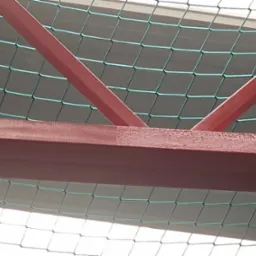 Metalowa konstrukcja pomalowana na czerwono, widoczna od dołu, z siatką zabezpieczającą w tle.