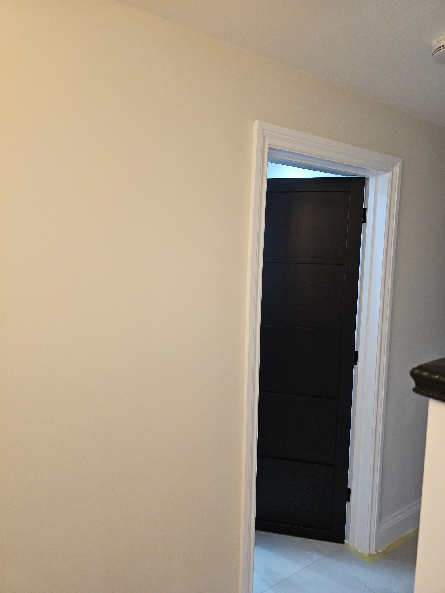 Świeżo pomalowane kremowe ściany z widocznym fragmentem czarnych, nowoczesnych drzwi z białymi ościeżnicami i szarą podłogą w tle.