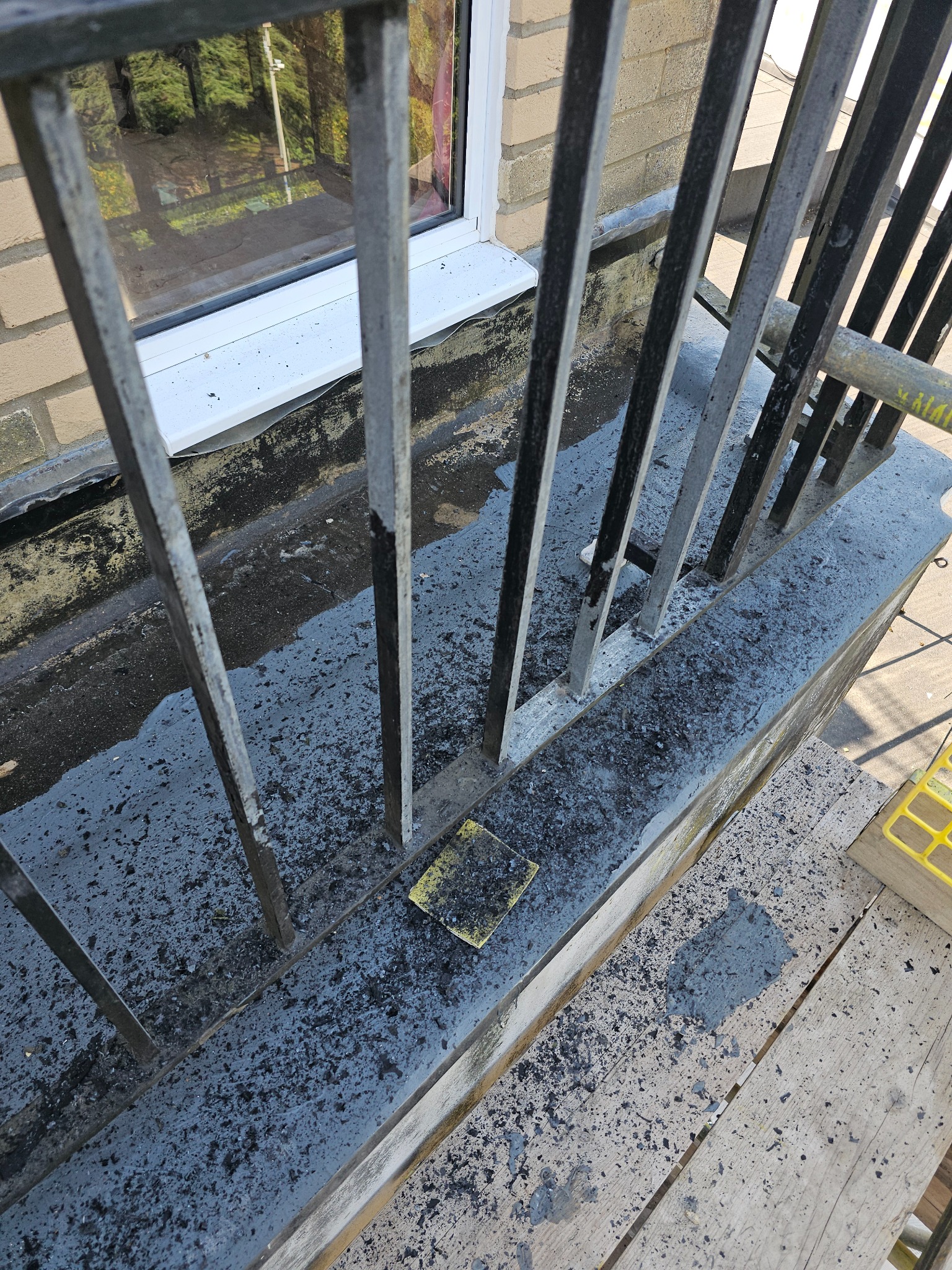 Metalowa balustrada balkonowa w trakcie czyszczenia z resztek starej farby, widoczna gąbka ścierna i fragment rusztowania.