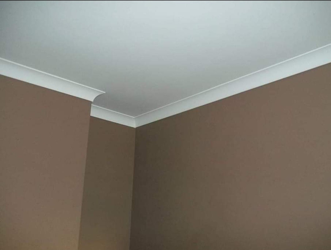 Brązowe ściany pomalowane matową farbą z białym, ozdobnym wykończeniem sufitu w rogu pokoju.