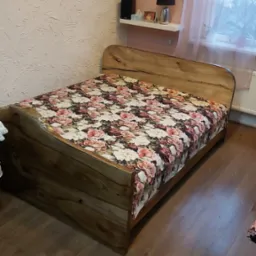 Drewniane łóżko z wyraźnym usłojeniem, nakryte pościelą w kwiaty, w sypialni z teksturalną ścianą i drewnianą podłogą.