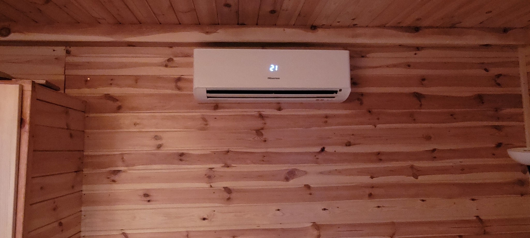 Biała jednostka klimatyzacji Hisense zamontowana na ścianie z boazerii w pomieszczeniu oświetlonym ciepłym światłem.