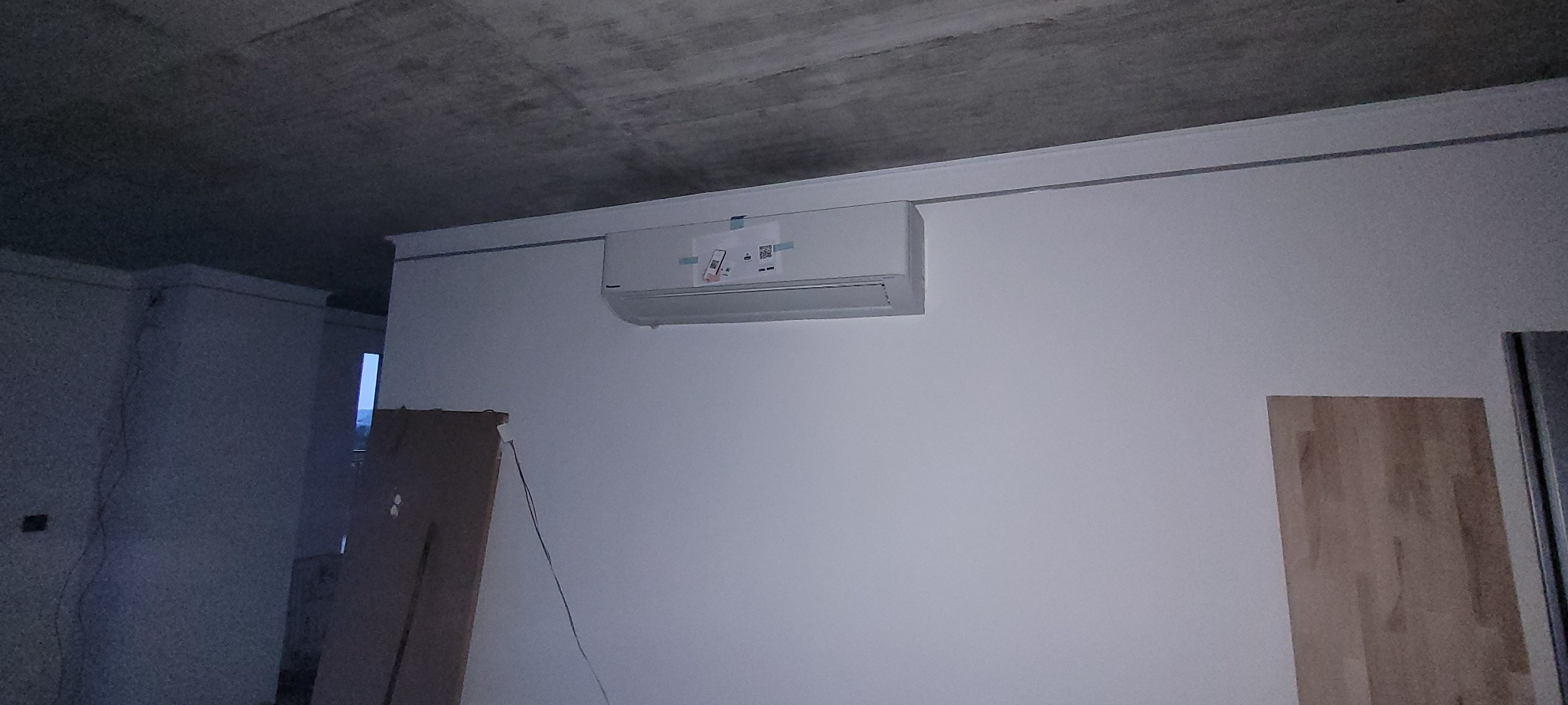 Nowo zamontowany klimatyzator na ścianie w surowym wnętrzu, z widocznymi etykietami producenta i surowym betonowym sufitem.