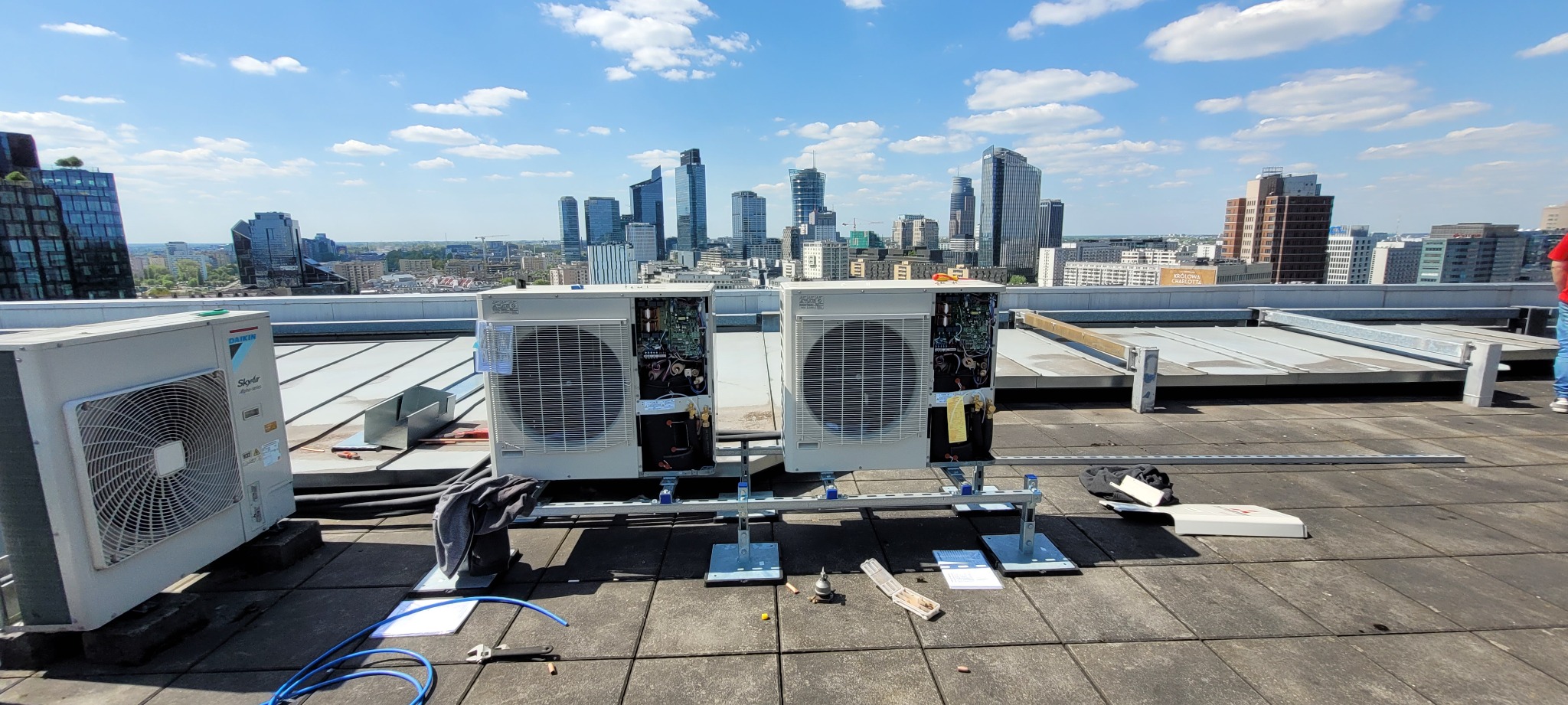 Montaż lub serwis klimatyzatorów Daikin na dachu budynku z widokiem na panoramę miasta w słoneczny dzień.