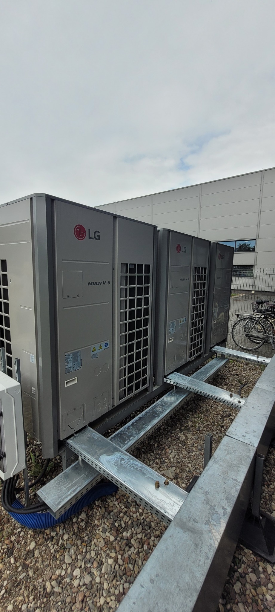 Cztery jednostki zewnętrzne klimatyzacji LG Multi V 5 ustawione na metalowej konstrukcji na dachu budynku, widoczne przewody i elementy montażowe.