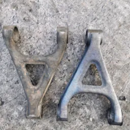 Dwa wahacze samochodowe typu A, jeden po lewej stronie z widocznymi śladami korozji i zabrudzeń, drugi po prawej stronie po procesie odnawiania z gładką, srebrną powłoką, leżą na szarej, kamiennej...