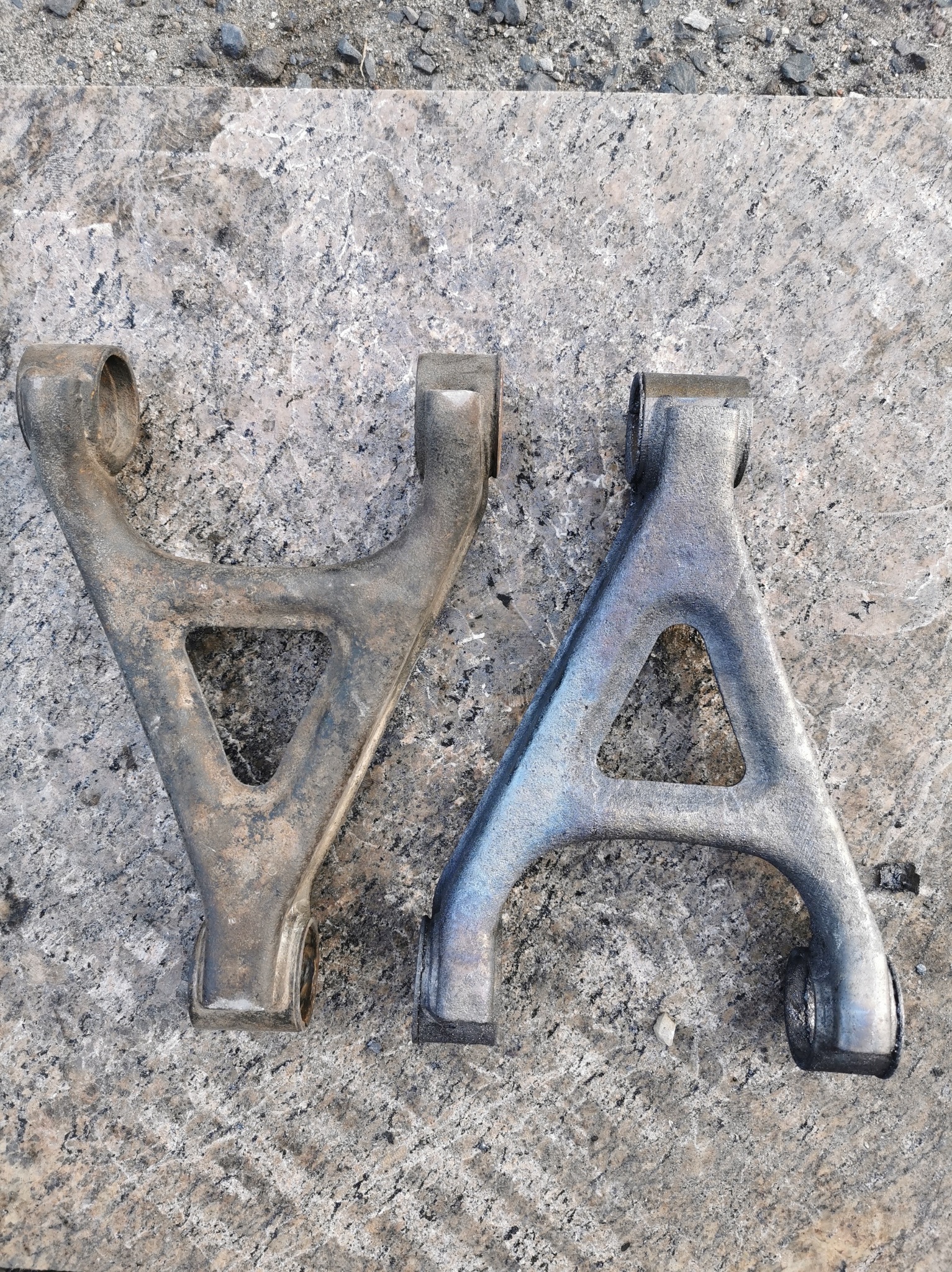 Dwa wahacze samochodowe typu A, jeden po lewej stronie z widocznymi śladami korozji i zabrudzeń, drugi po prawej stronie po procesie odnawiania z gładką, srebrną powłoką, leżą na szarej, kamiennej...