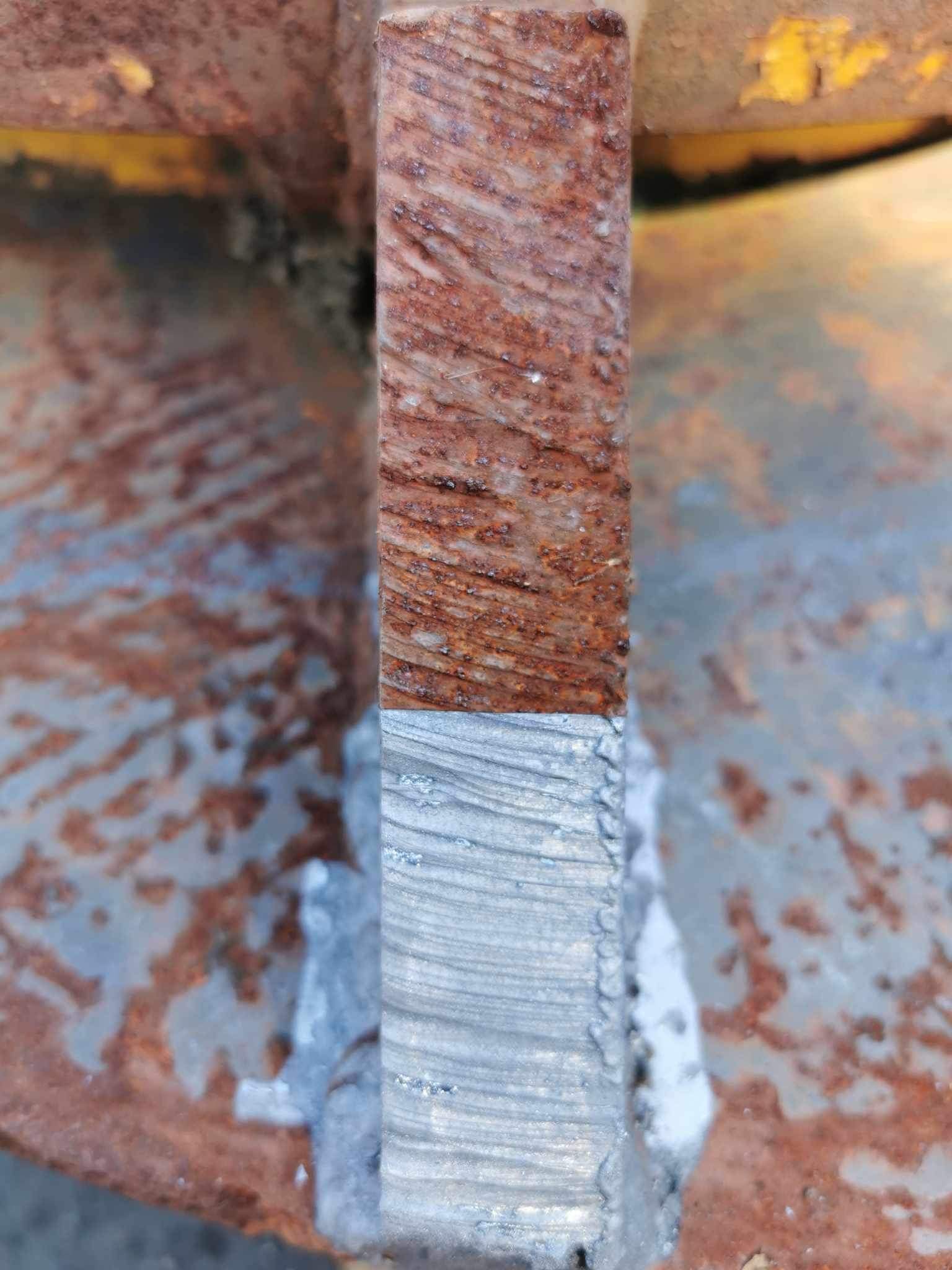 Metalowy element z widoczną rdzą na górnej połowie i oczyszczoną, srebrzystą powierzchnią na dolnej połowie, ukazujący efekt obróbki.